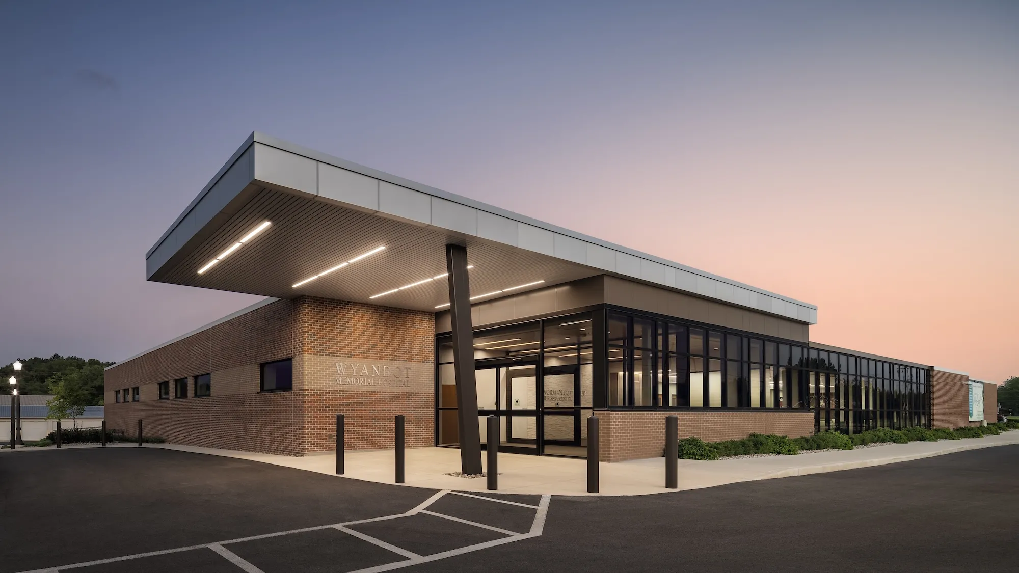 Exterior entrance of Wyandot Memorial Hospital at dusk, one story building featuring brick walls and floor to ceiling windows