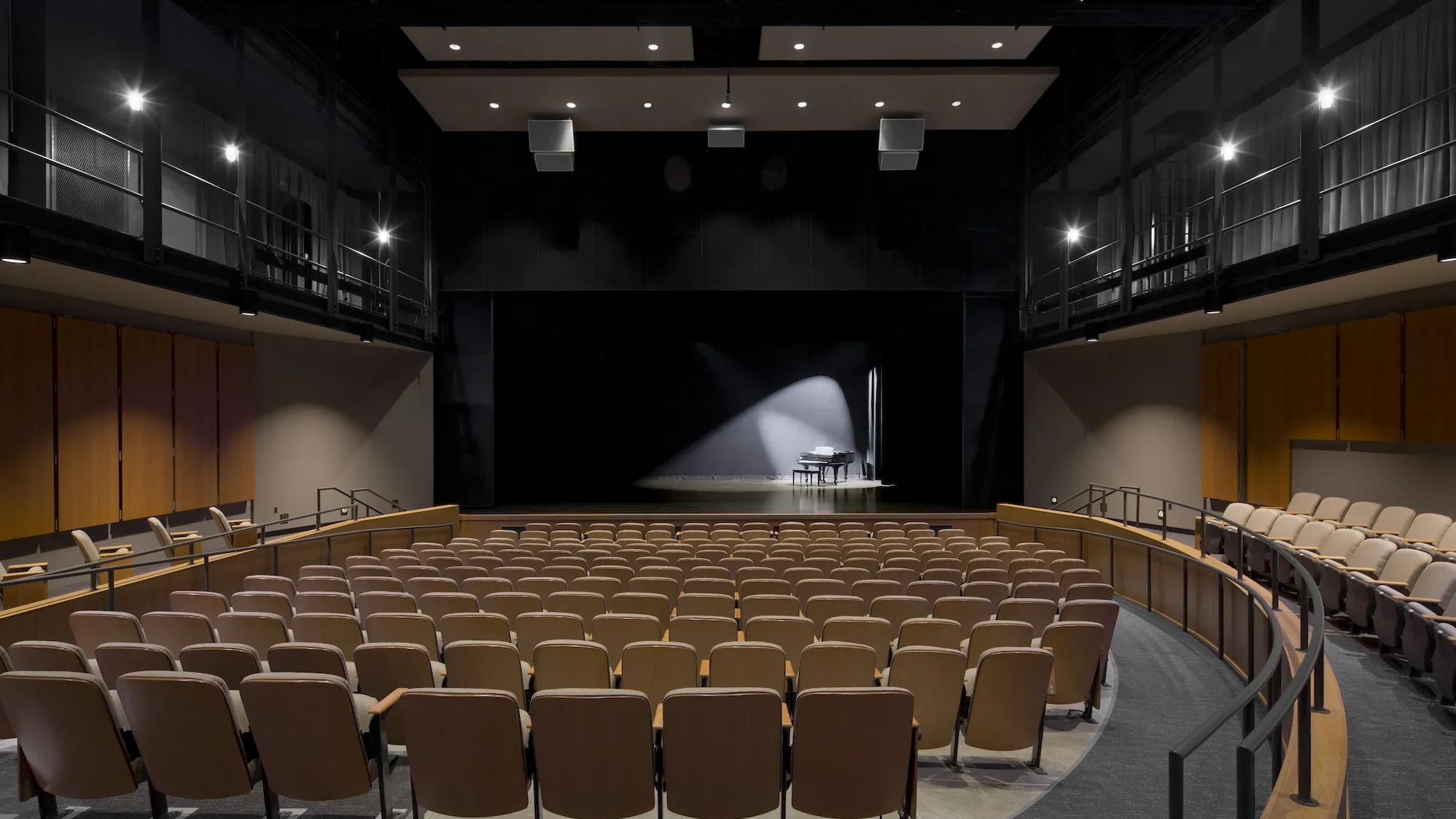 Interior of a theater seats with a piano on stage with a spotlight on it