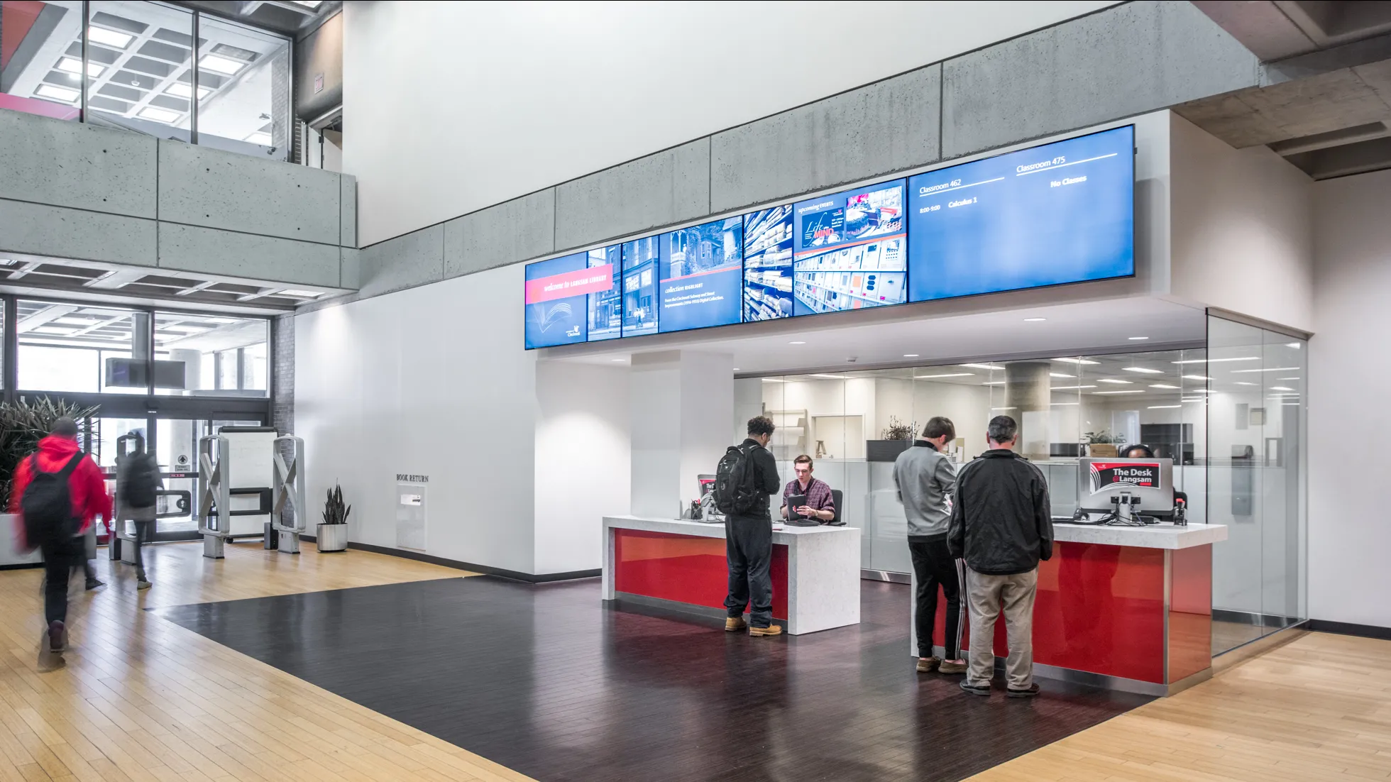 Interior of Langsam library check out desks, featuring wood paneled floors, white and red accents