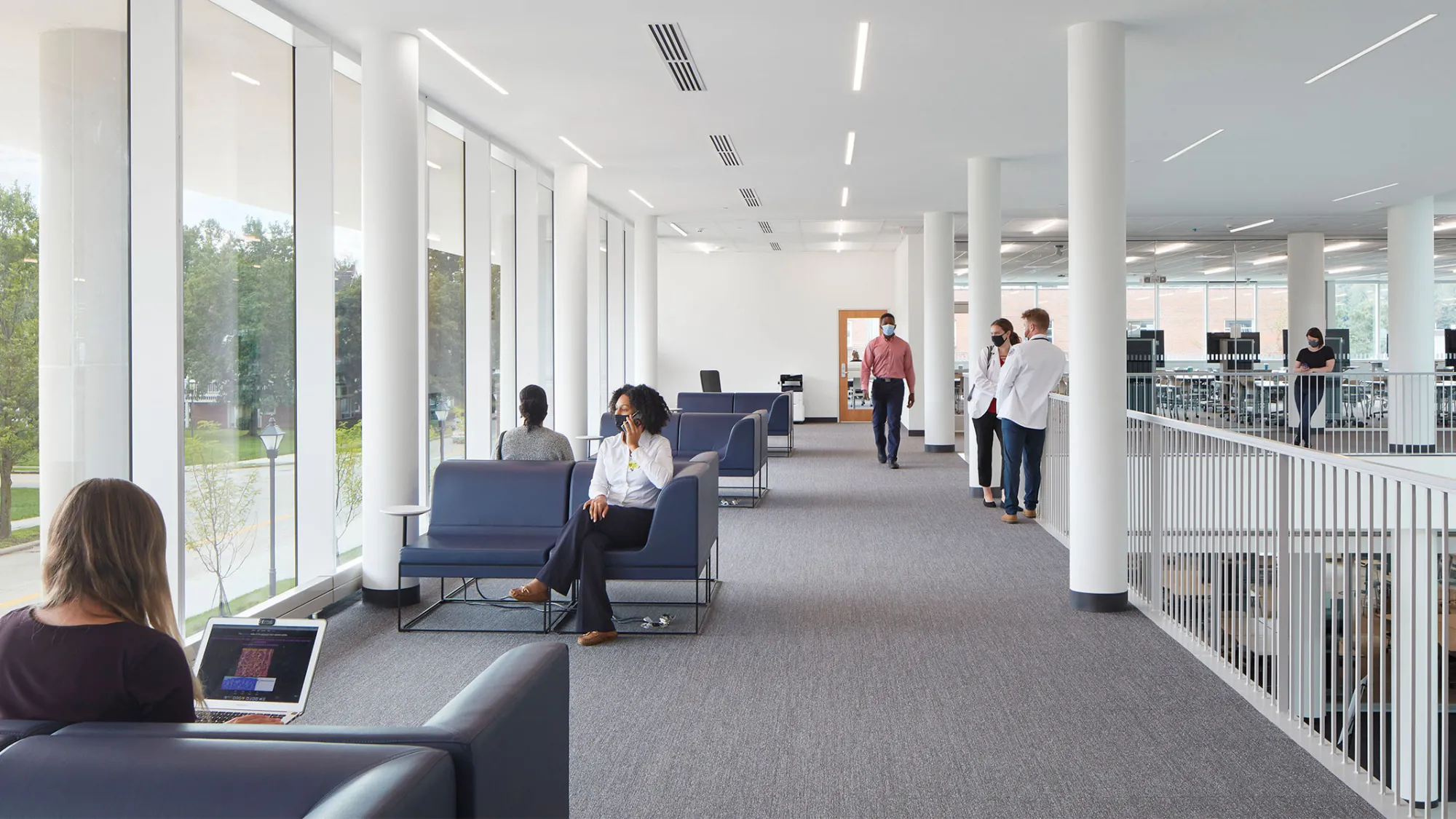 People in a brightly and natural lit waiting area in a medical facility.