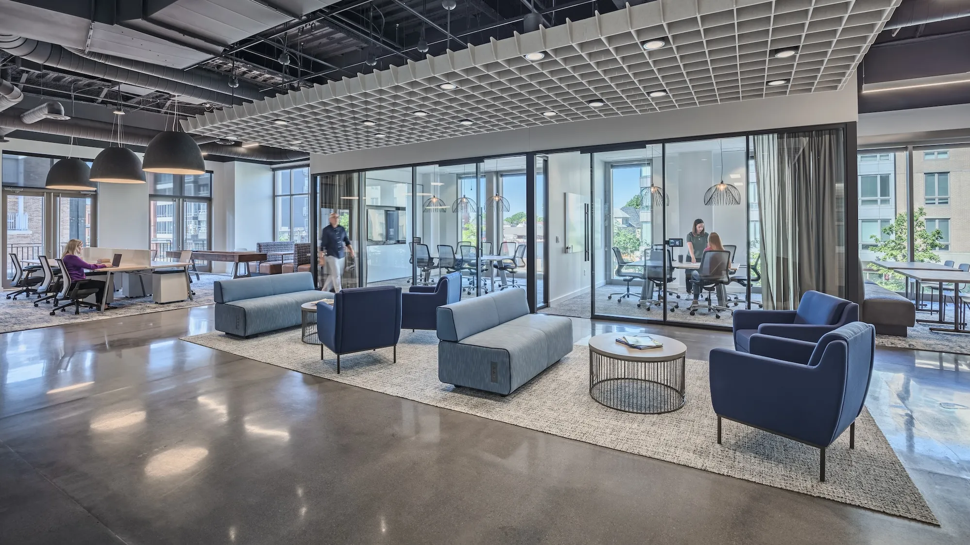 Interior of a modern workplace with all glass conference rooms, couches and chairs that are gray and blue.