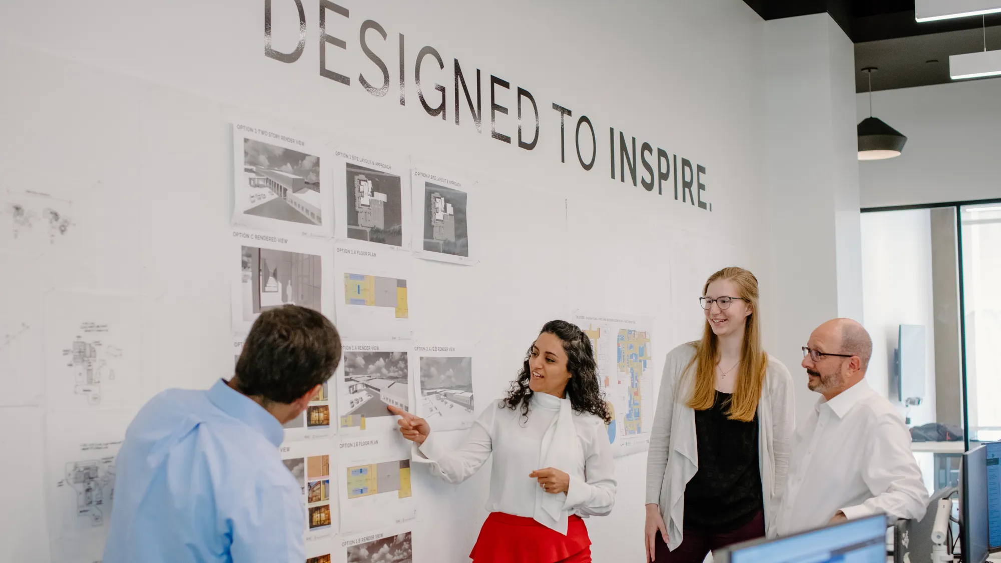 A group of people standing at a wall that says "Designed to Inspire"