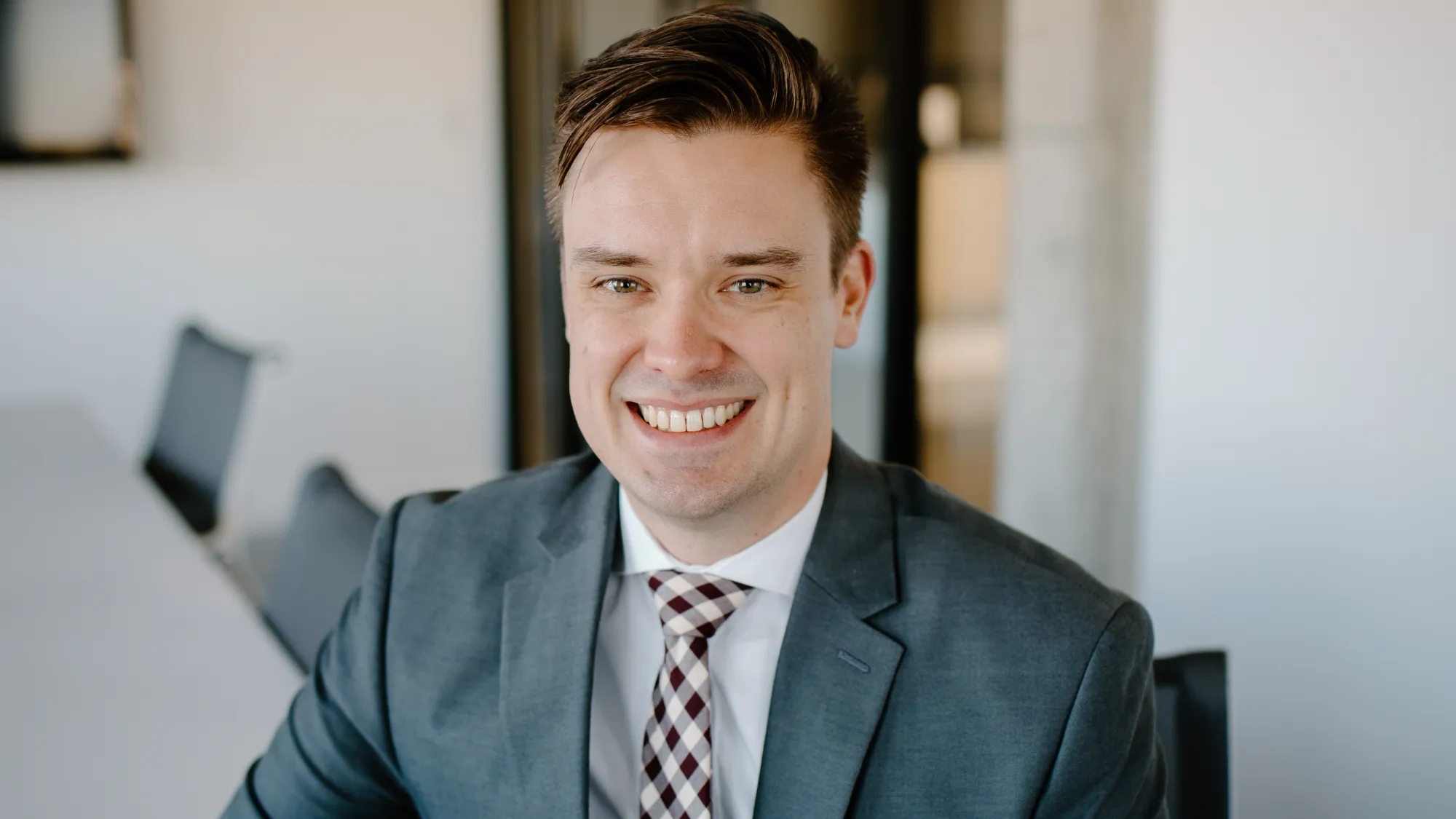 A man with brown hair, wearing a suit and smiling