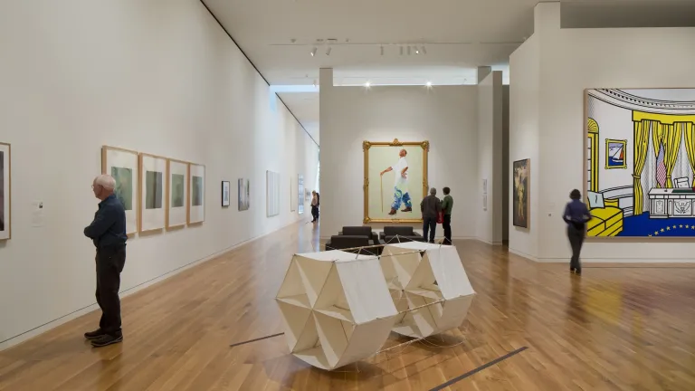 Interior of Columbus Museum of Art, variety of large art pieces on the walls as well as sculptures in the center of the room with people taking it all in