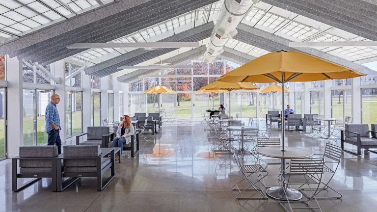 Daytime enclosed glass extension of the Hilliard Library that houses various patio furnishing, a park surrounding the exterior