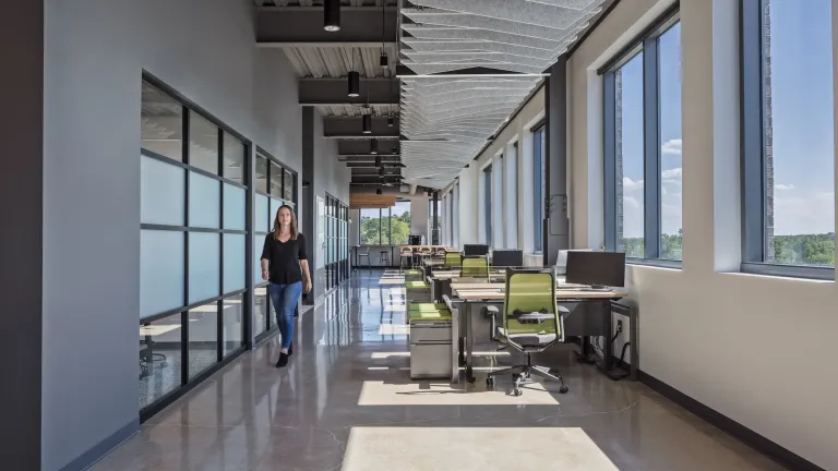 A corridor with desks lining a wall of windows and conference rooms on the other side