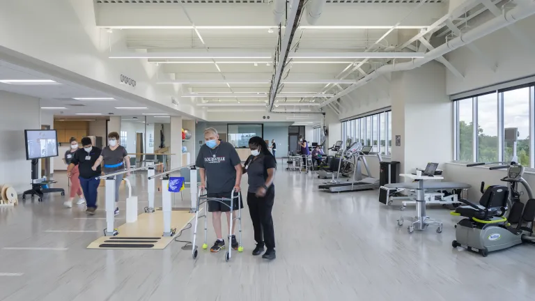 Physical rehab space featuring a nurse helping a man with a walker surrounded by exercise equipment