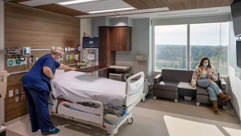 Nurse making a bed in a patient's room, featuring modern wood paneling and light blue accents