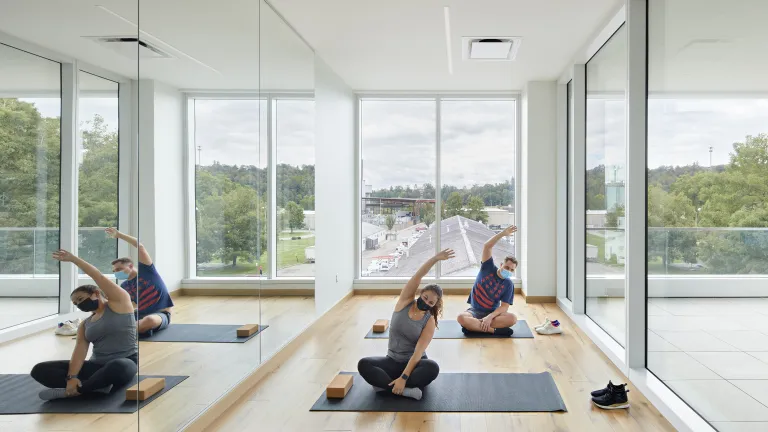 Two people in a naturally lit room doing stretches on yoga mats.