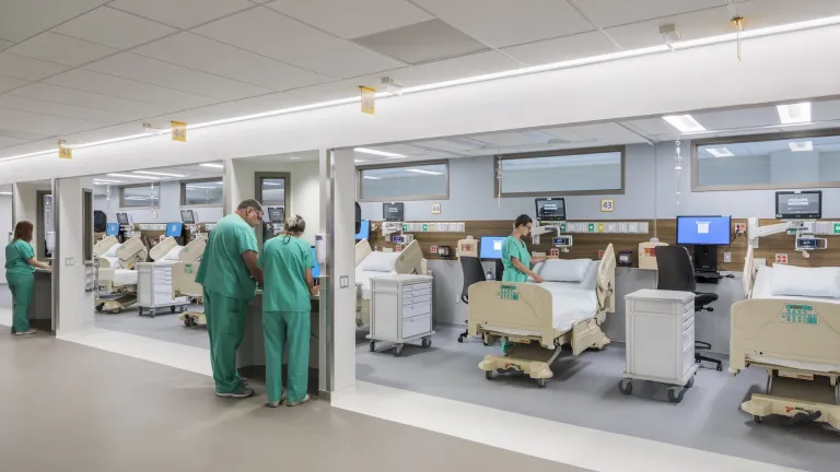 Interior of a patient bay space with multiple beds and people in blue scrubs