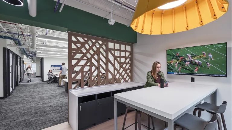 Kitchen dining space within the Pittsburgh University IT office, featuring a yellow hanging light and television.