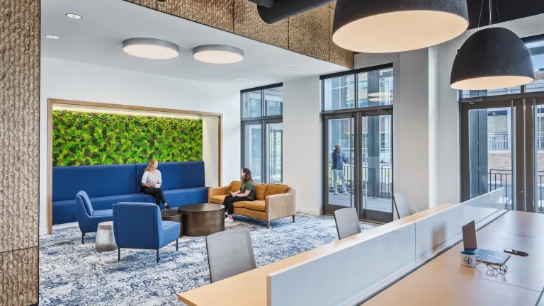 Lobby space of a mixed use workplace, featuring blue and leather couches, big blue area rug, and large shared desk space