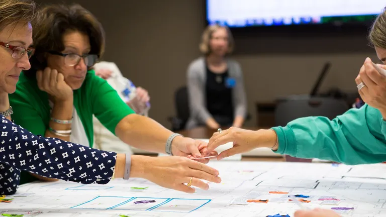 A group of clinical staff reaching across and interacting with a blueprint on a table