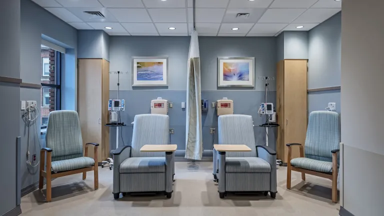 Interior of patient room space with four blue cushioned chairs and a curtain room divider