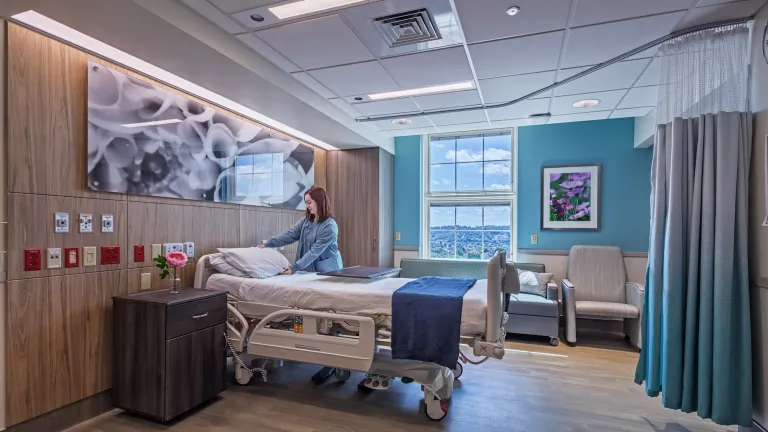 Patient room with wood walls and blue accents, a nurse making the bed