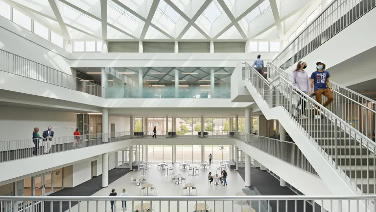 Large, natural lit atrium with tables and people walking through the space through the three floors.