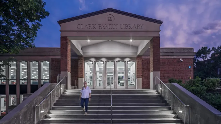 Front entrance engraved with "Clark Family Library" as a woman walks down the steps