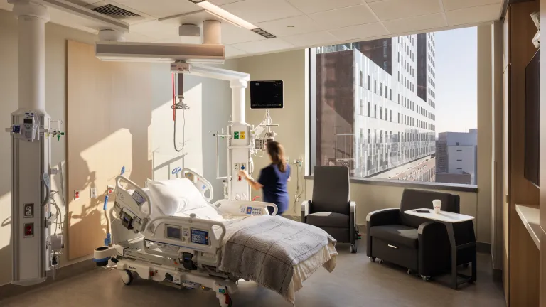 nurse preparing equipment in intensive care unit patient room filled with natural light and wood accents