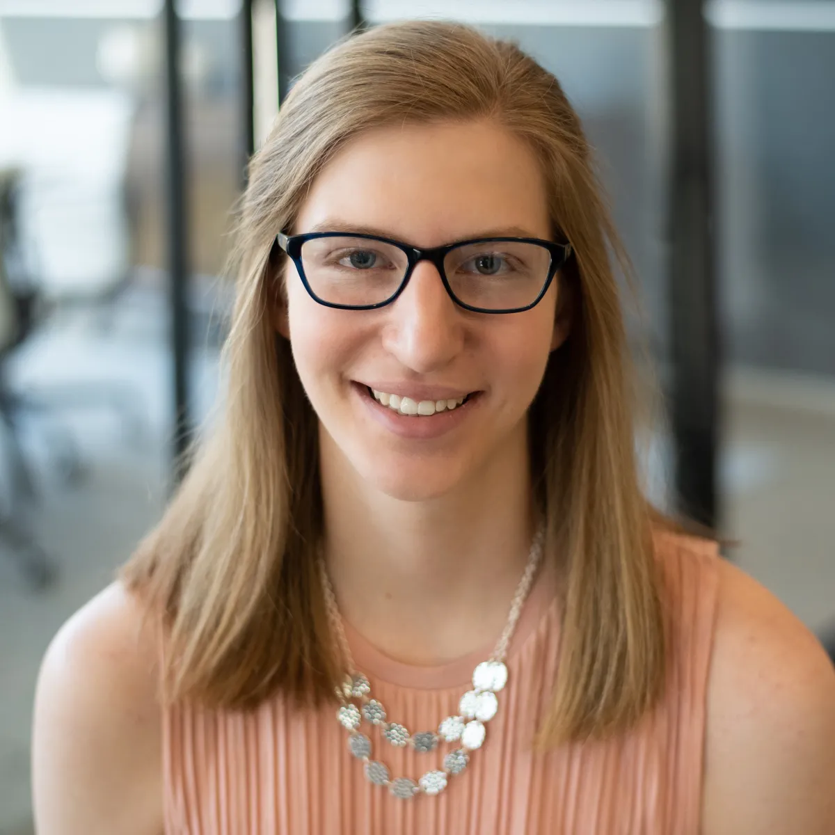 Emily Wagner smiling, wearing a pink blouse and statement necklace