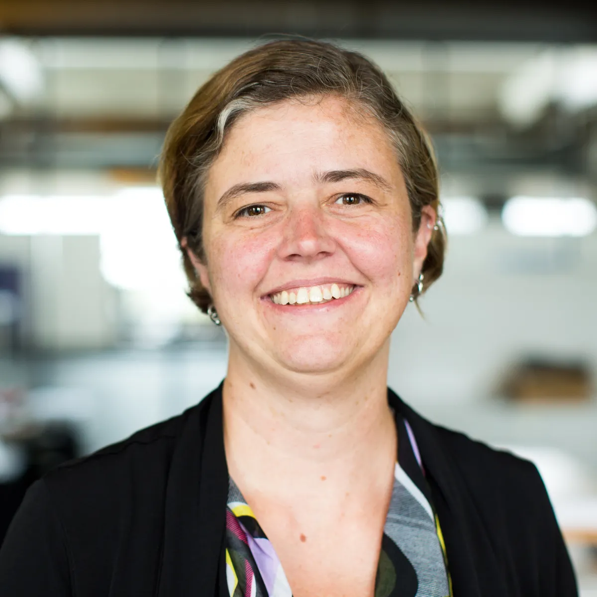 Jamie Oxier smiling, wearing a black blazer and multi-colored blouse