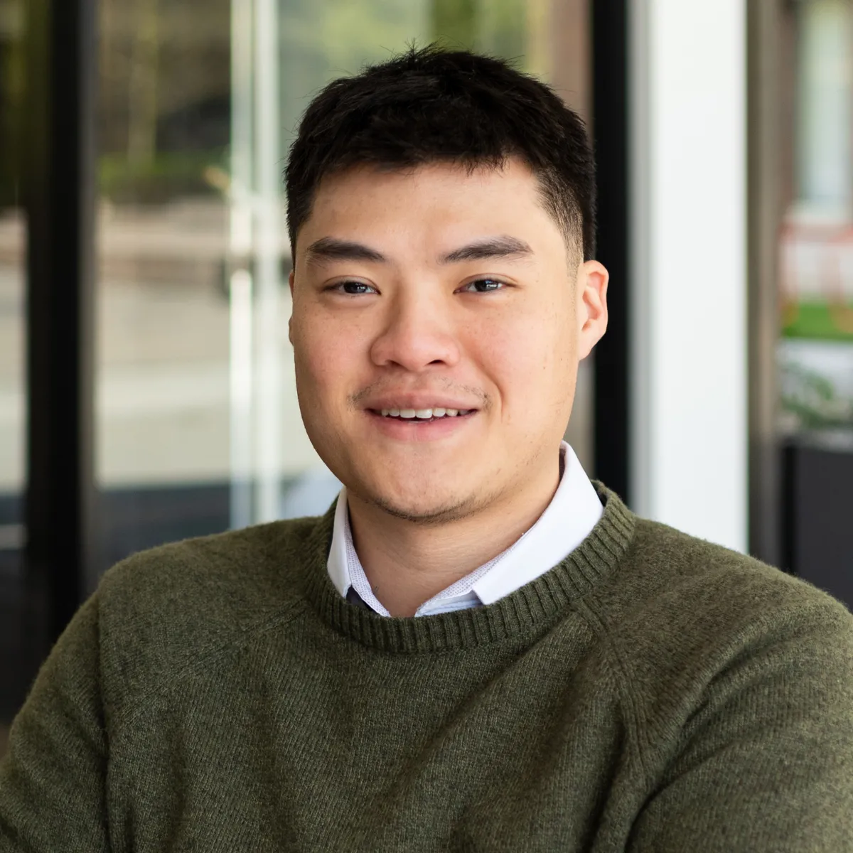 Longney Luk smiling, wearing a green sweater with white button down underneath