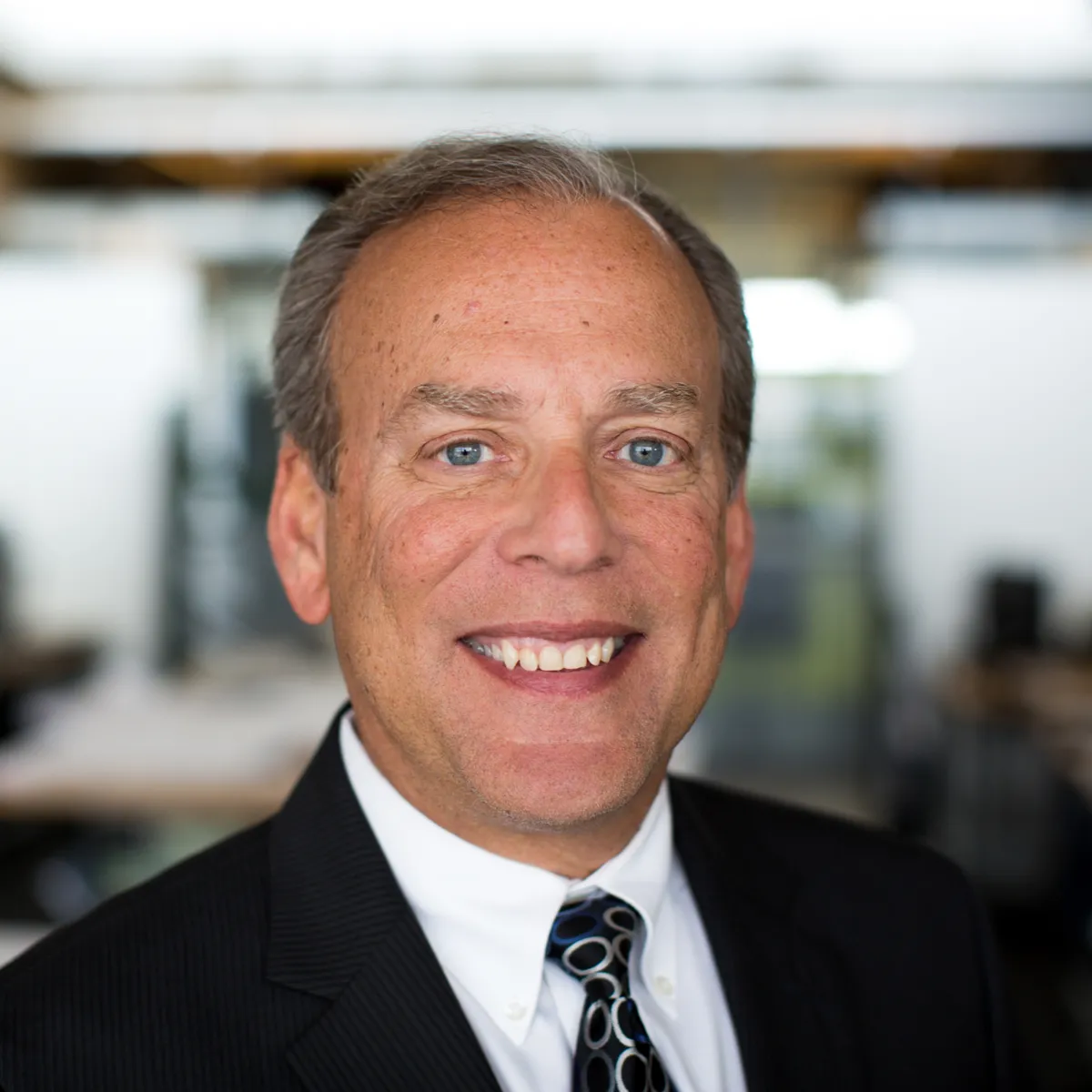 Lorne Eisen smiling while wearing a black blazer, white shirt and black and silver embossed tie