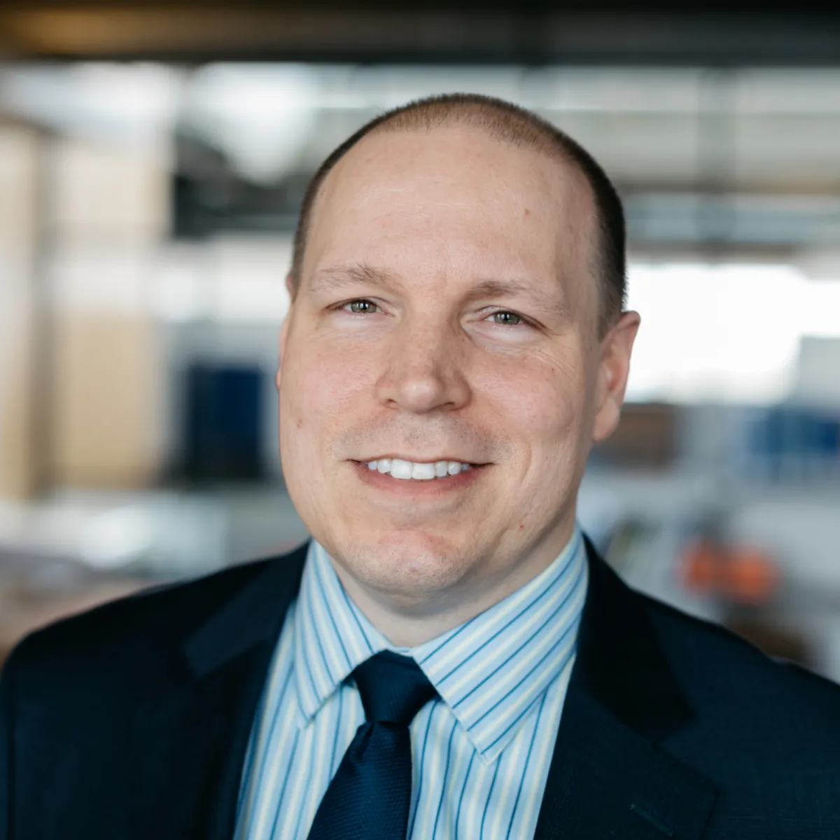 Rick Rodman smiling, wearing a navy blazer and blue striped shirt with navy tie
