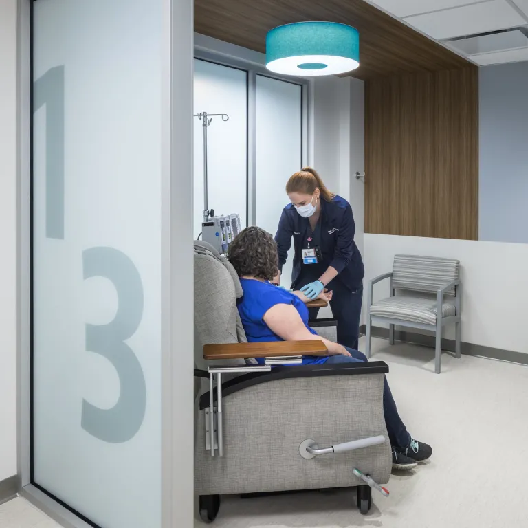 Nurse performing a blood transfusion on a patient in a modern room with wood paneling and blue accents