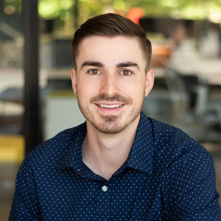 Alex Keiser smiling, wearing a navy polka dot button down shirt