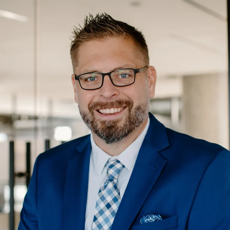 Chris Haedt smiling while wearing a blue blazer and blue gingham tie