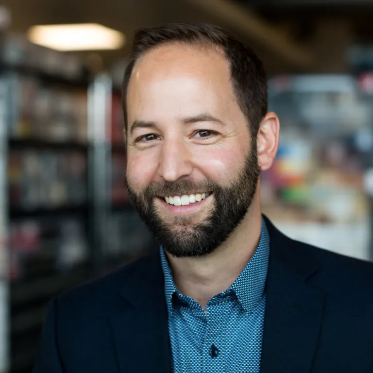 Mike Forejt smiling while wearing a dark navy blazer and teal shirt