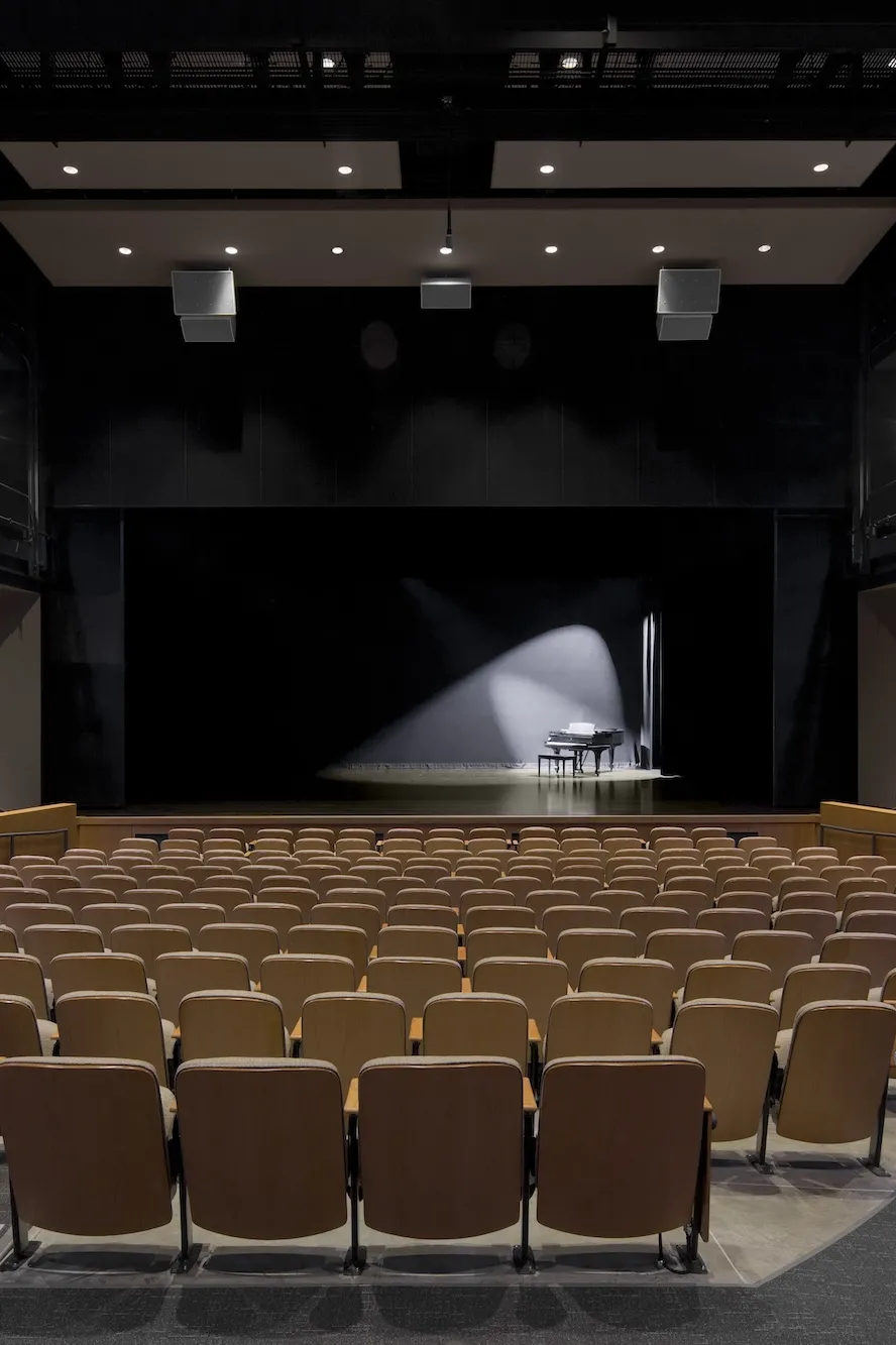 Interior of a theater seats with a piano on stage with a spotlight on it