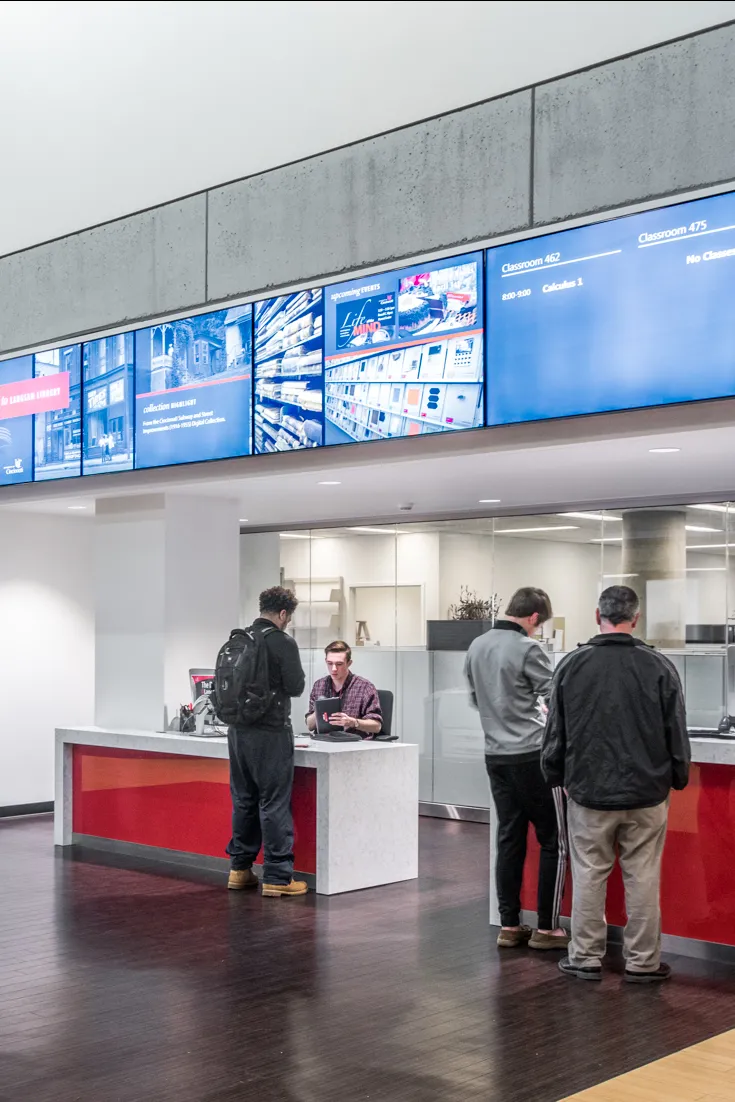 Interior of Langsam library check out desks, featuring wood paneled floors, white and red accents