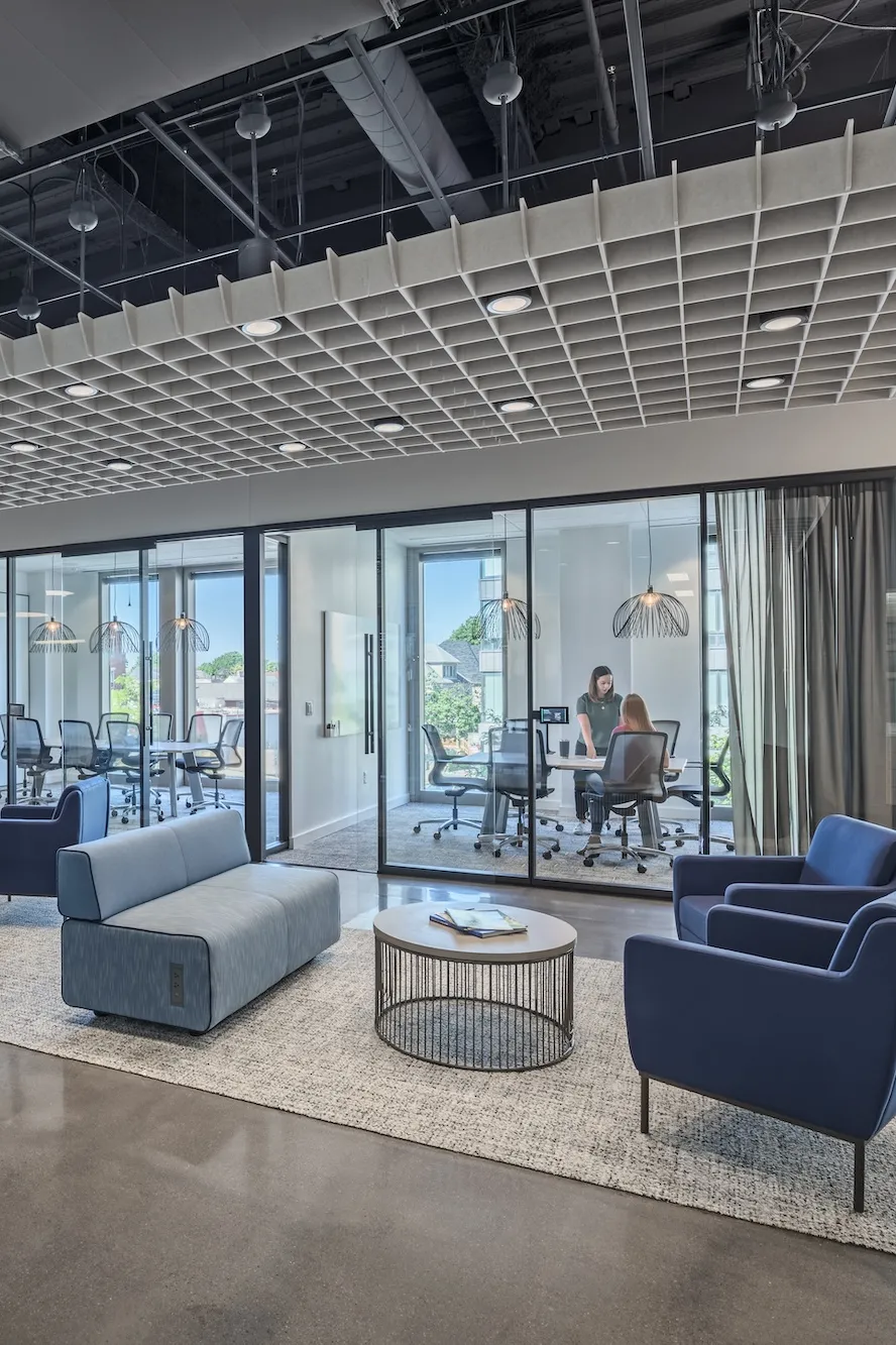 Interior of a modern workplace with all glass conference rooms, couches and chairs that are gray and blue.