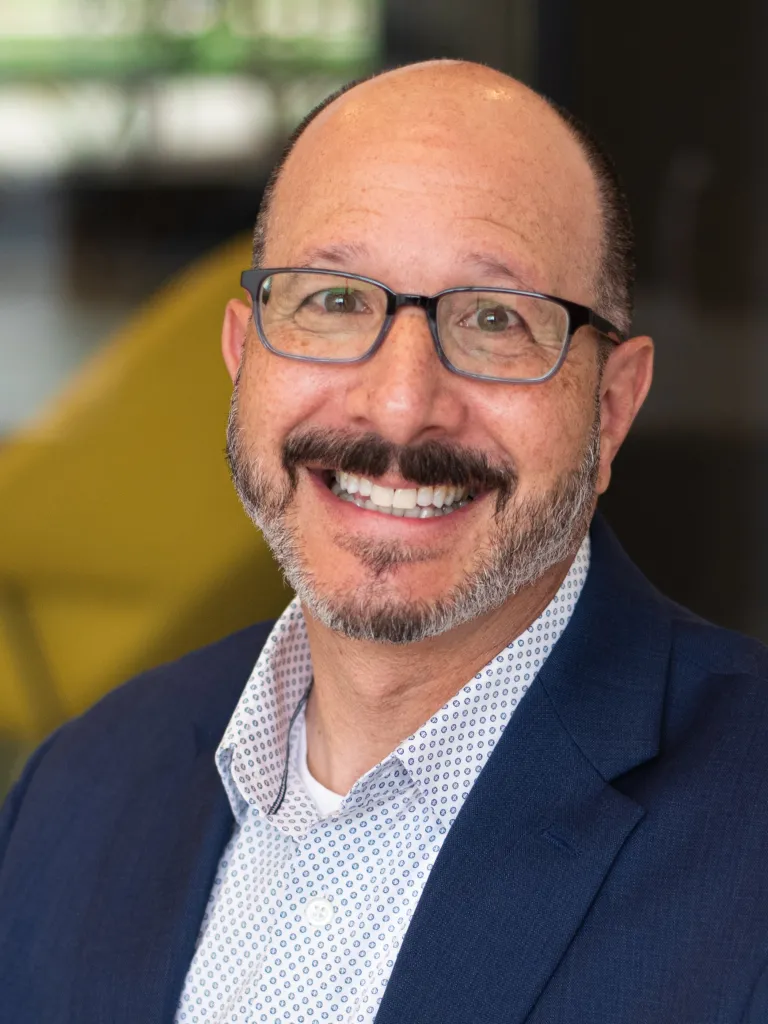 Alan Schlossberg smiling while wearing a navy blazer and blue shirt