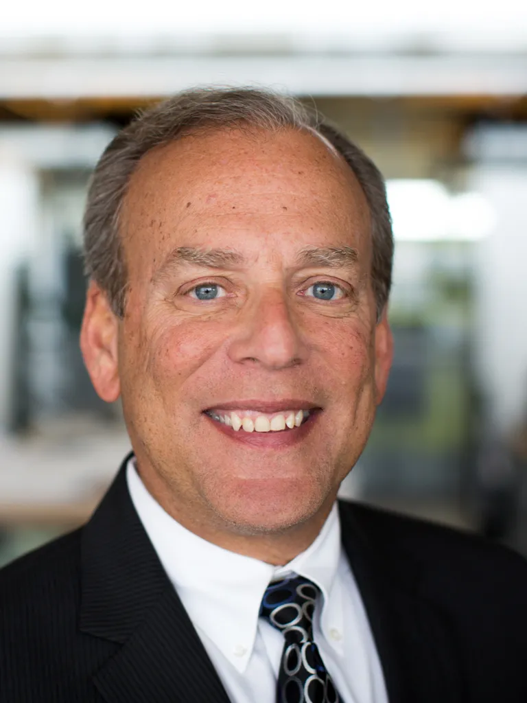 Lorne Eisen smiling while wearing a black blazer, white shirt and black and silver embossed tie