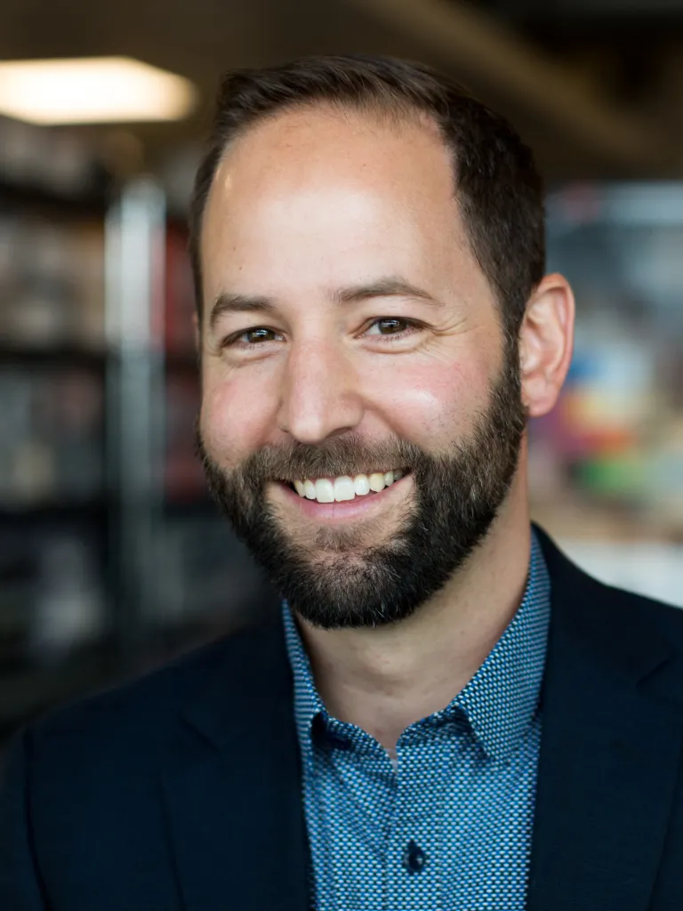 Mike Forejt smiling while wearing a dark navy blazer and teal shirt