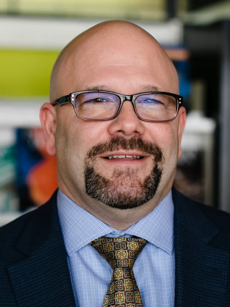 Tom Stanko smiling, wearing a navy blazer and blue shirt