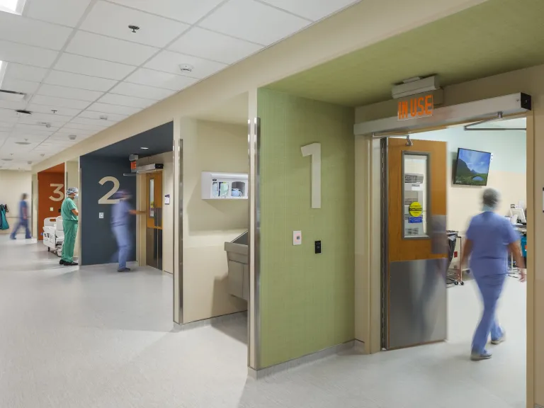 Interior of a hospital hallway featuring rooms one, two, and three and each wall outside the rooms are a different color: green, blue, orange