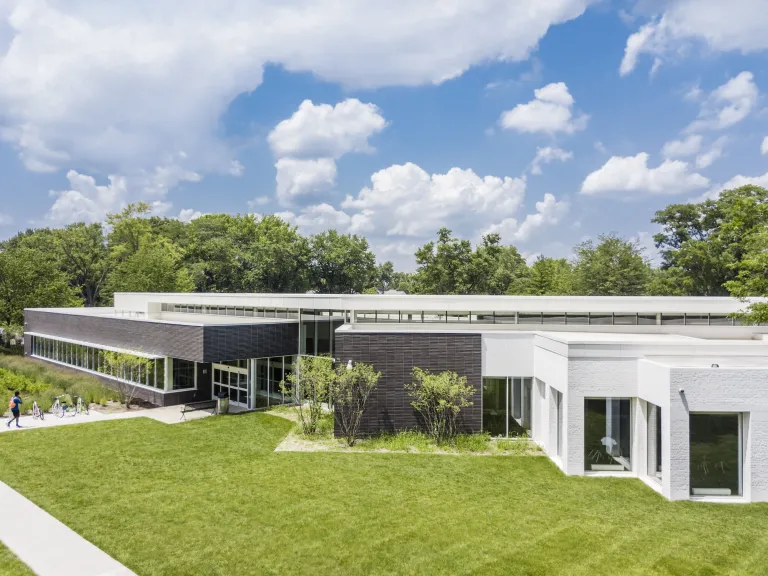 Exterior of Northern Lights Columbus Library during the day, a modern and gray one story building standing brightly amongst greenery and a blue cloudy sky