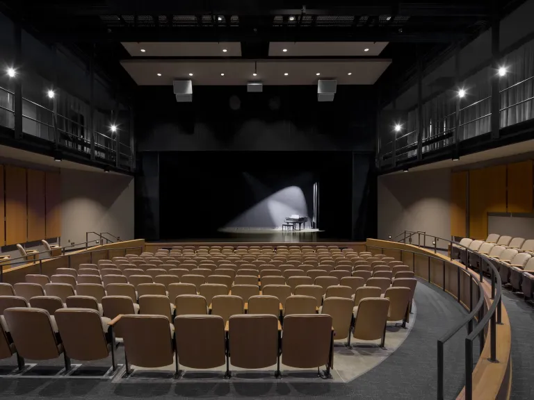 Interior of a theater seats with a piano on stage with a spotlight on it