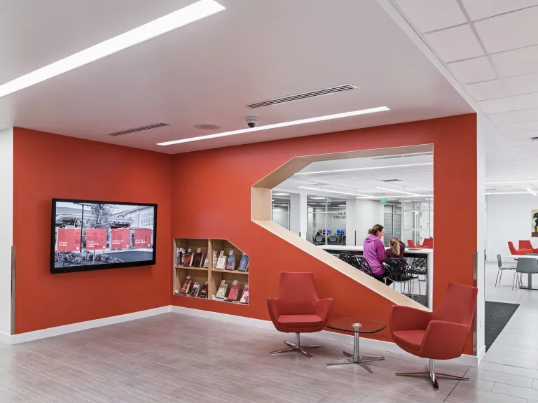 Interior of Hilliard Library, focusing on a corner nook that is painted a warm orange with matching cushioned chairs and television