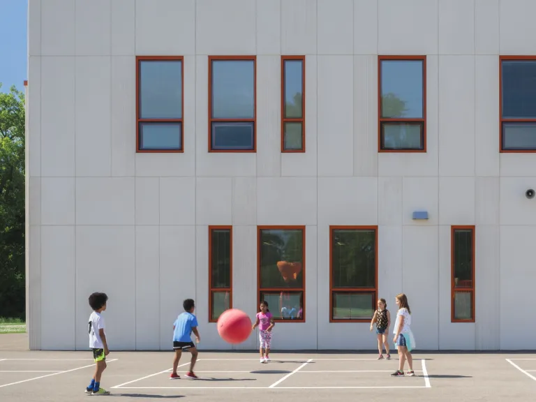 Children playing with a big red ball against the facade of the Columbus Spanish Immersion Academy