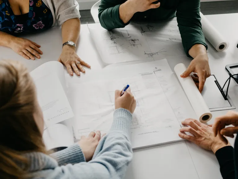 Over the shoulder view of architects collaborating on plans around a table.