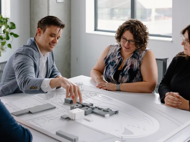 A smiling man adjusts a model building on the table while three other employees watch