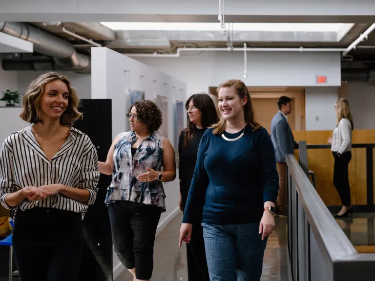 Several DG employees in the hall of their office, conversing and walking around