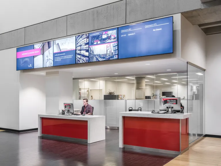 Interior of Langsam library check out desks, featuring wood paneled floors, white and red accents