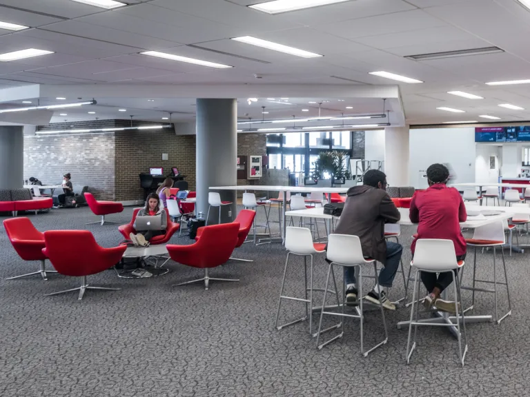 Large open space near the front entrance of the Langsam library, featuring students at variety of red and white tables and chairs