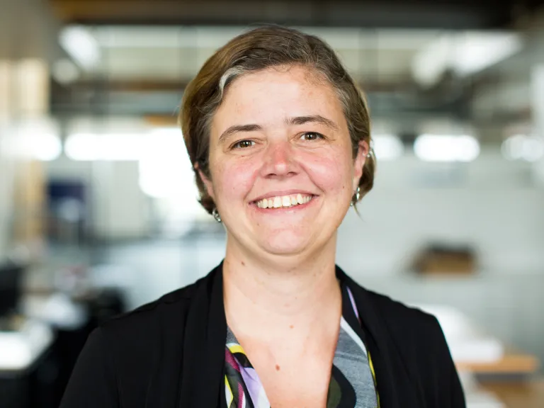 Jamie Oxier smiling, wearing a black blazer and multi-colored blouse