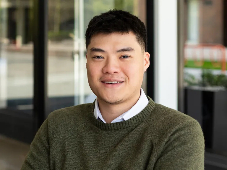 Longney Luk smiling, wearing a green sweater with white button down underneath